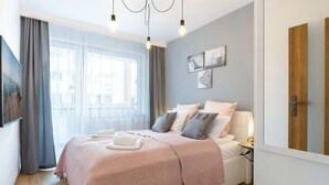A modern bedroom with a large bed, a bedside table, a mirror, and a window with curtains.