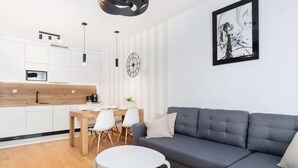 A modern kitchen with white cabinets, a wooden countertop, and a dining area with a gray sofa and a small white table.