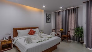 Ein Hotelzimmer mit einem ordentlich bezogenen Bett, einem Nachttisch mit Telefon, einem kleinen Tisch mit Pflanze und einem Sessel.