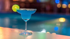 Ein blauer Cocktail mit Limettenscheibe an einer Bar neben einem Pool.