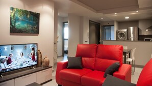 Un salon moderne avec un canapé rouge, un téléviseur à écran plat et un tableau représentant une scène de forêt.