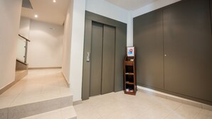 Un couloir avec un escalier, une paire de portes doubles et une petite étagère en bois sur laquelle est posée une pancarte.
