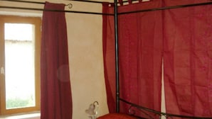Ein Zimmer mit einem Bett, einem Fenster mit Vorhängen und einem Metallbettgestell.