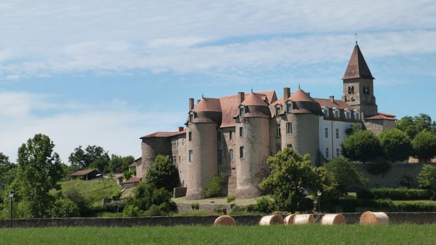 Eine historische Burg mit mehreren Türmen und einer Kirche, umgeben von Grünflächen und Feldern.