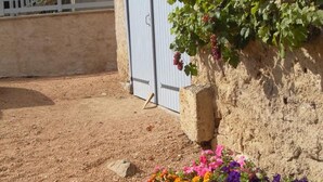 Eine Scheune mit Erdboden, einem weißen Zaun und einer Mauer mit einem Blumenbeet voller bunter Blumen und Weinreben.