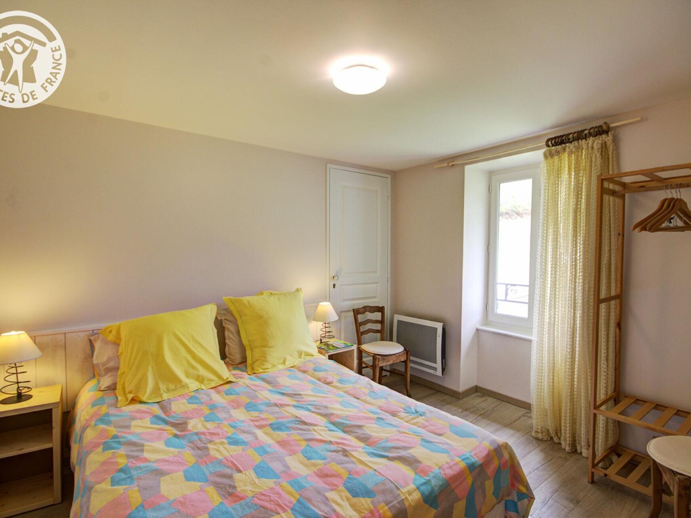 Une chambre à coucher comprenant un lit, des tables de chevet, une chaise, un bureau, un téléviseur et une fenêtre avec des rideaux.