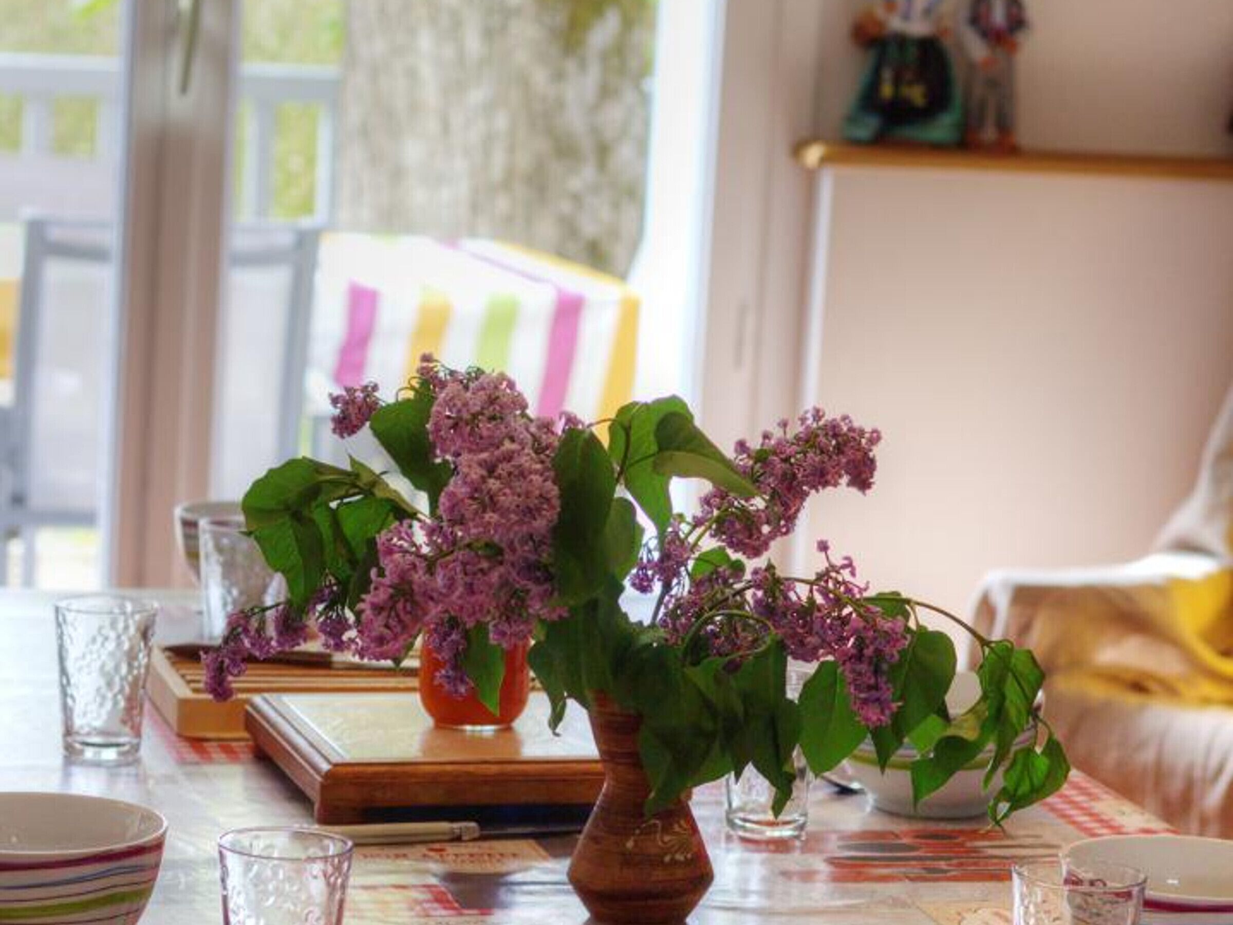 A table with a vase of lilac flowers, books, and glasses.