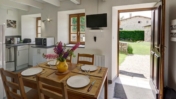 Une cuisine moderne avec des meubles blancs, une table à manger pour quatre personnes et un téléviseur fixé au mur.