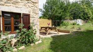 Un edificio de piedra con ventana de madera y una mesa de picnic en el patio.