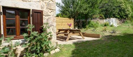 A stone building with a wooden window and a picnic table in the yard.