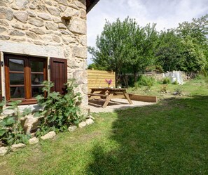 Un edificio de piedra con ventana de madera y una mesa de picnic en el patio.