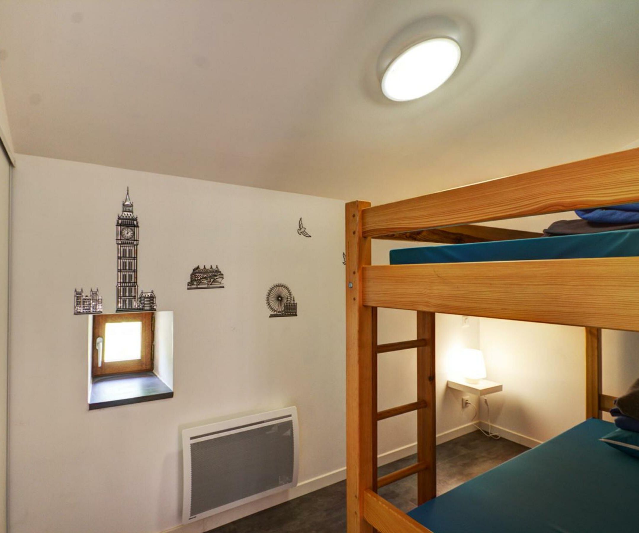 Dormitorio con literas, ventana, radiador y adornos en la pared, incluyendo un reloj y una torre.