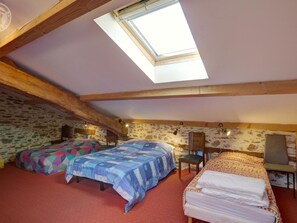 A cozy attic bedroom with two beds, a skylight, stone walls, and a rustic wooden ceiling.