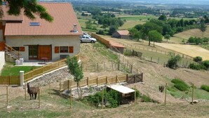 Une maison avec un toit en tuiles, une cour clôturée et une vue sur la campagne.