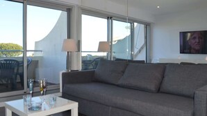 A modern living room with a grey sofa, a small white coffee table, and a TV mounted on the wall.