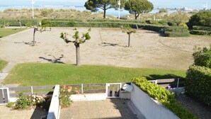 A landscaped area with a paved path, a small garden with roses, and a view of the sea and distant buildings.