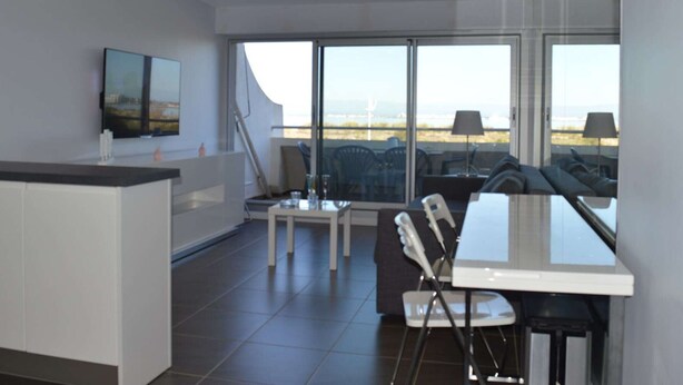 A modern kitchen with a large island, a dining area with a glass table and chairs, and large windows offering a view of the landscape.