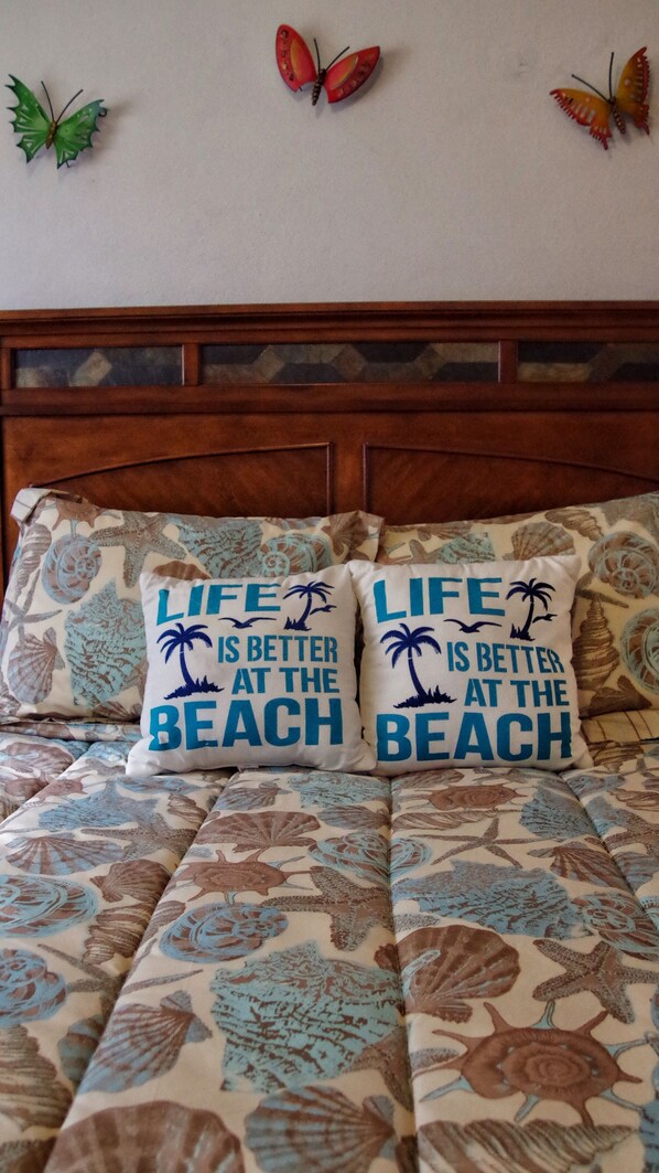 Un letto con una coperta a tema spiaggia e due cuscini con la scritta "LIFE IS BETTER AT THE BEACH".