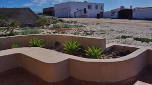 A desert landscape with white buildings, a paved area, and small green plants in a concrete planter.