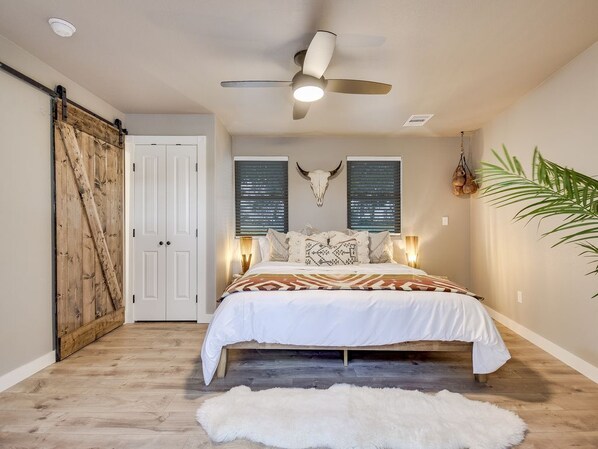Quarto com cama, ventilador de teto, porta branca e uma planta.