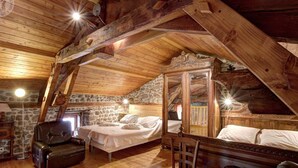 Una camera da letto rustica in mansarda, con travi a vista in legno, una parete in pietra, un letto di legno, una poltrona in pelle e un armadio di legno.