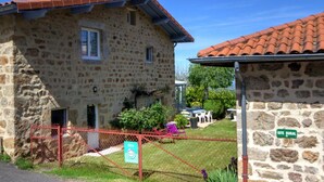 A stone building with a red-tiled roof, a fenced yard, and a sign indicating 'GITE RURAL'. - Gîte Bellevue in Marols for 6 people with charming enclosed yard (Marols)