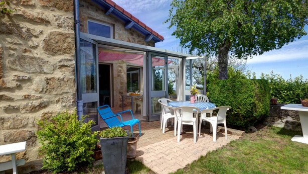 A stone building with a glass-enclosed patio, outdoor seating, and a tree. - Gîte Bellevue in Marols for 6 people with charming enclosed yard (Marols)