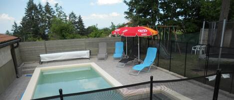 Una piscina con zona techada, sillas de descanso y sombrillas.