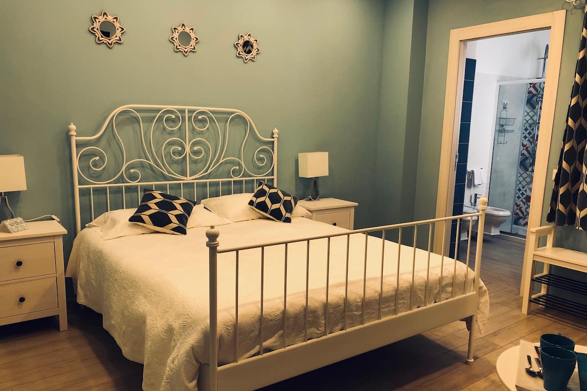 A bedroom with a white metal bed frame, two bedside tables with lamps, and a nightstand with a phone.