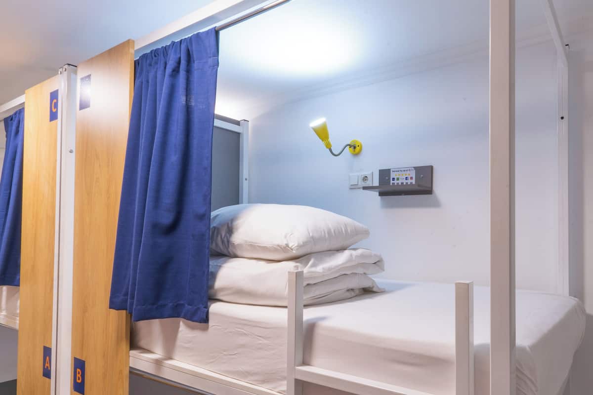 A bunk bed with a headboard, a bedside table with a lamp, and a control panel on the wall.