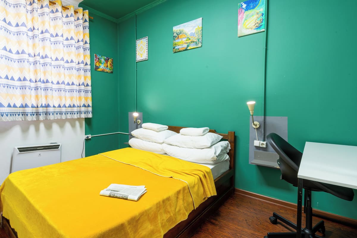 A room with a bed, a desk, a chair, a wall-mounted lamp, and artwork.