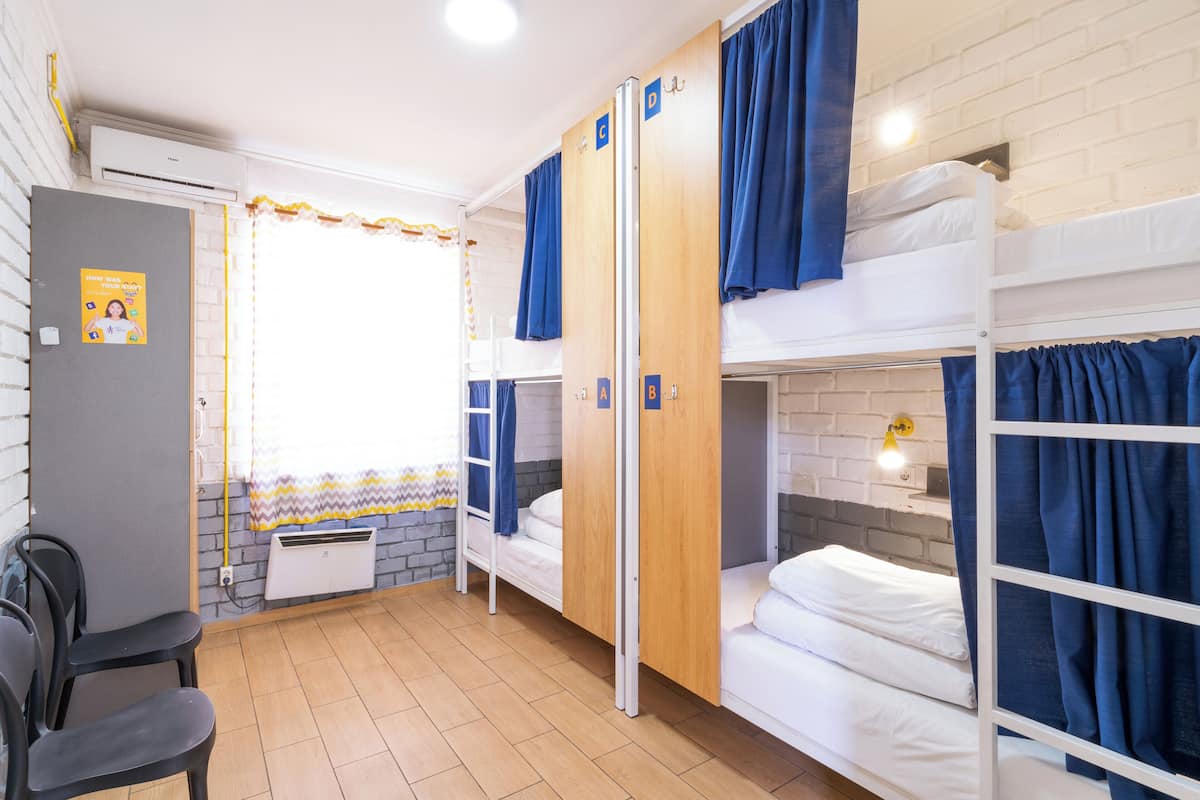 A dormitory room with bunk beds, a radiator, a window with curtains, and a chair.