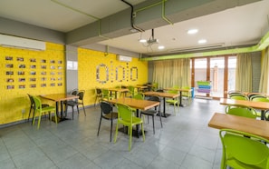 A brightly lit dining area with yellow brick walls, green and black chairs, and multiple tables. - Freelander Work and Travel Hostel (Bishkek)