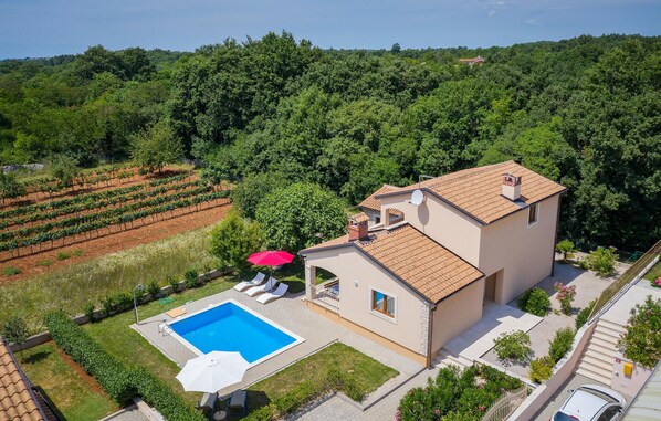 Ein zweistöckiges Haus mit Schwimmbad, umgeben von einem Garten und einem Weinberg.