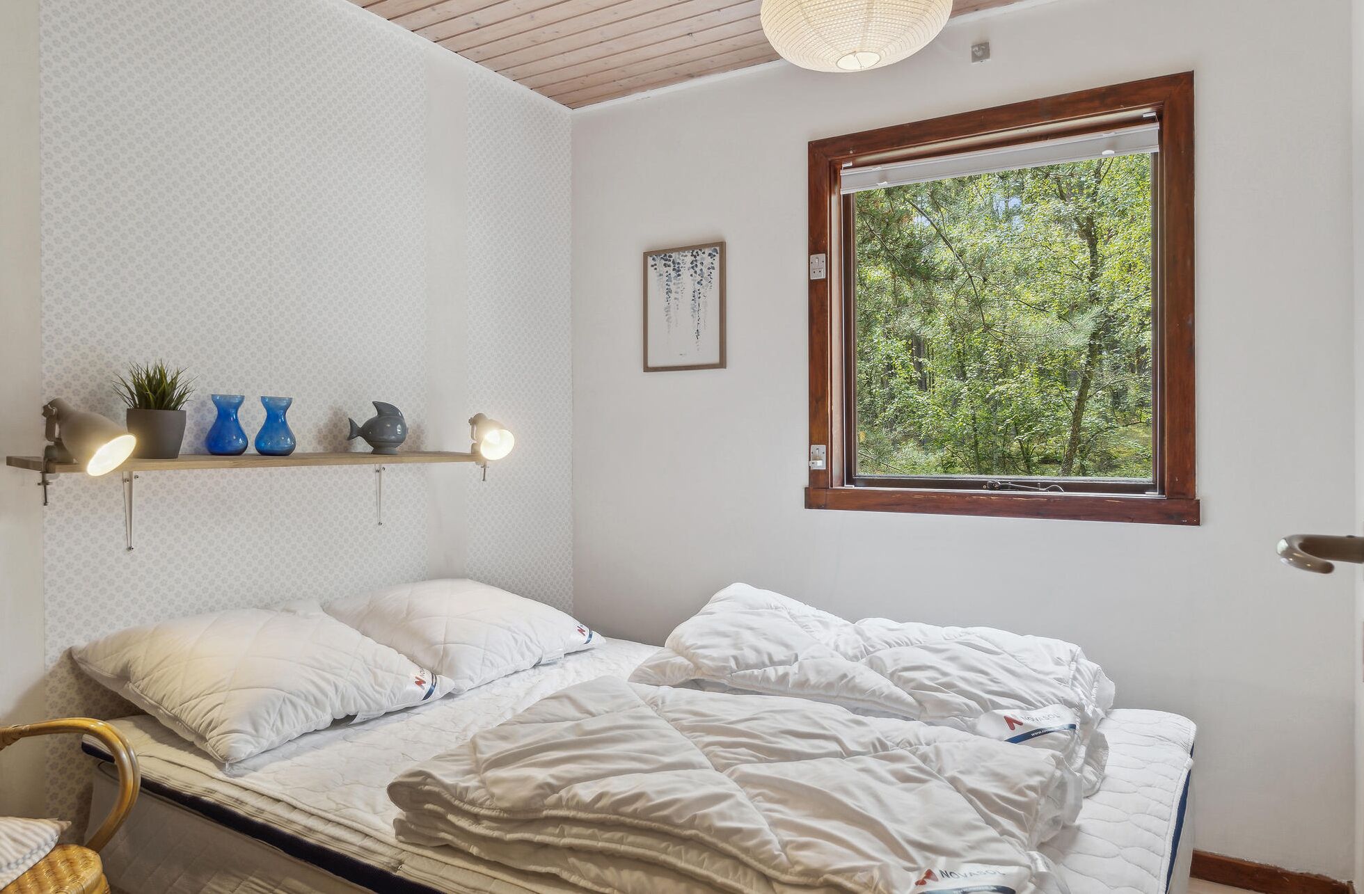 Ein Schlafzimmer mit einem Bett, einem Fenster mit Blick auf Bäume, einer Ablage mit Dekoration und einer Wand mit geometrischem Muster.