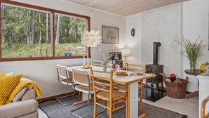 A cozy room with a dining table, chairs, a sofa, a fireplace, and a large window overlooking a forest. - Stunning home in Nexø with WiFi (Nexø)