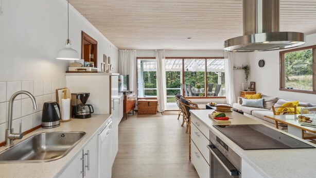 A modern kitchen with a large window, a dining area with a table and chairs, and a built-in oven. - Stunning home in Nexø with WiFi (Nexø)