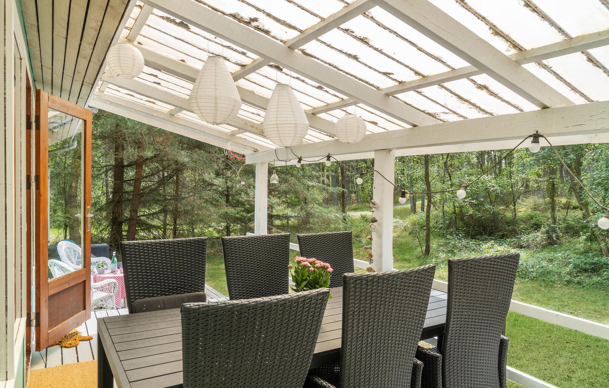 A covered patio with wicker furniture and a view of the forest.