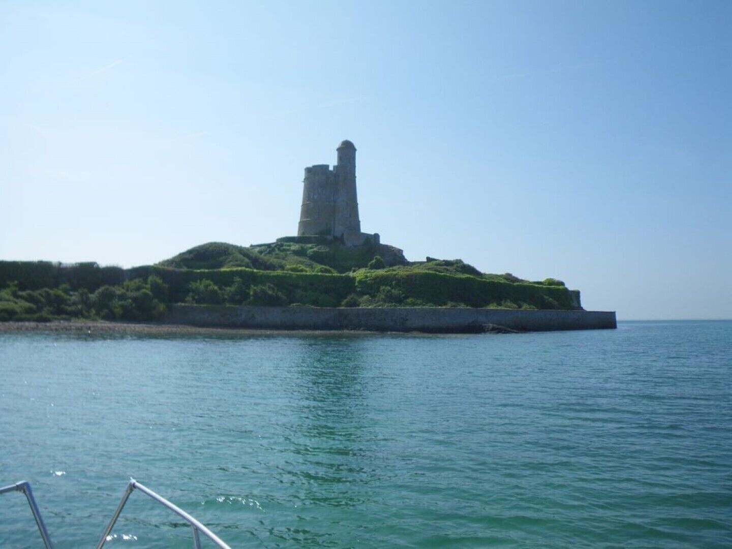 A coastal fortification with a prominent tower, surrounded by greenery and overlooking the sea.