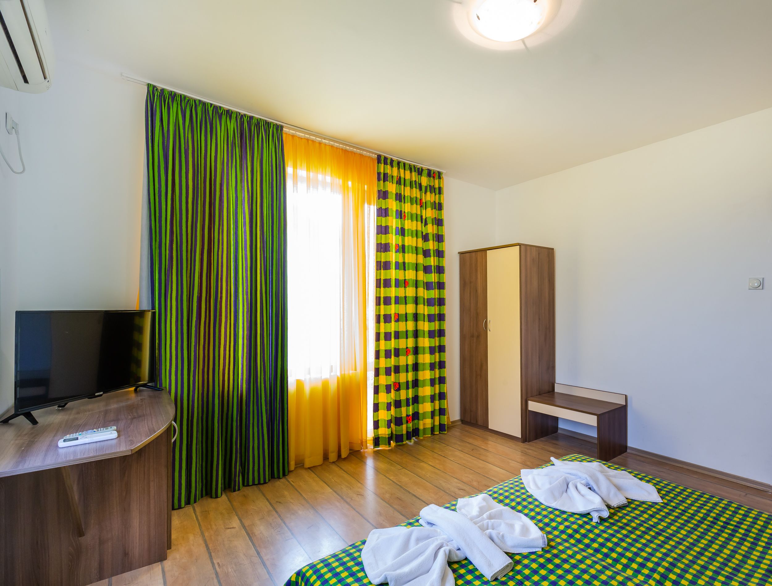 Hotellihuone, jossa on sänky, televisio, vaatekaappi ja työpöytä.