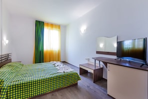 A hotel room with a bed, a desk, a TV, and a window with curtains.