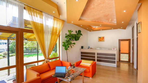 A modern living room with orange sofas, a glass coffee table, and a laptop. - 2 Bedroom Apartment in Dafinka Guest House (Ravda)