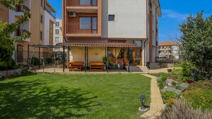 A multi-story residential building with a covered outdoor seating area and a well-maintained lawn. - 2 Bedroom Apartment in Dafinka Guest House (Ravda)