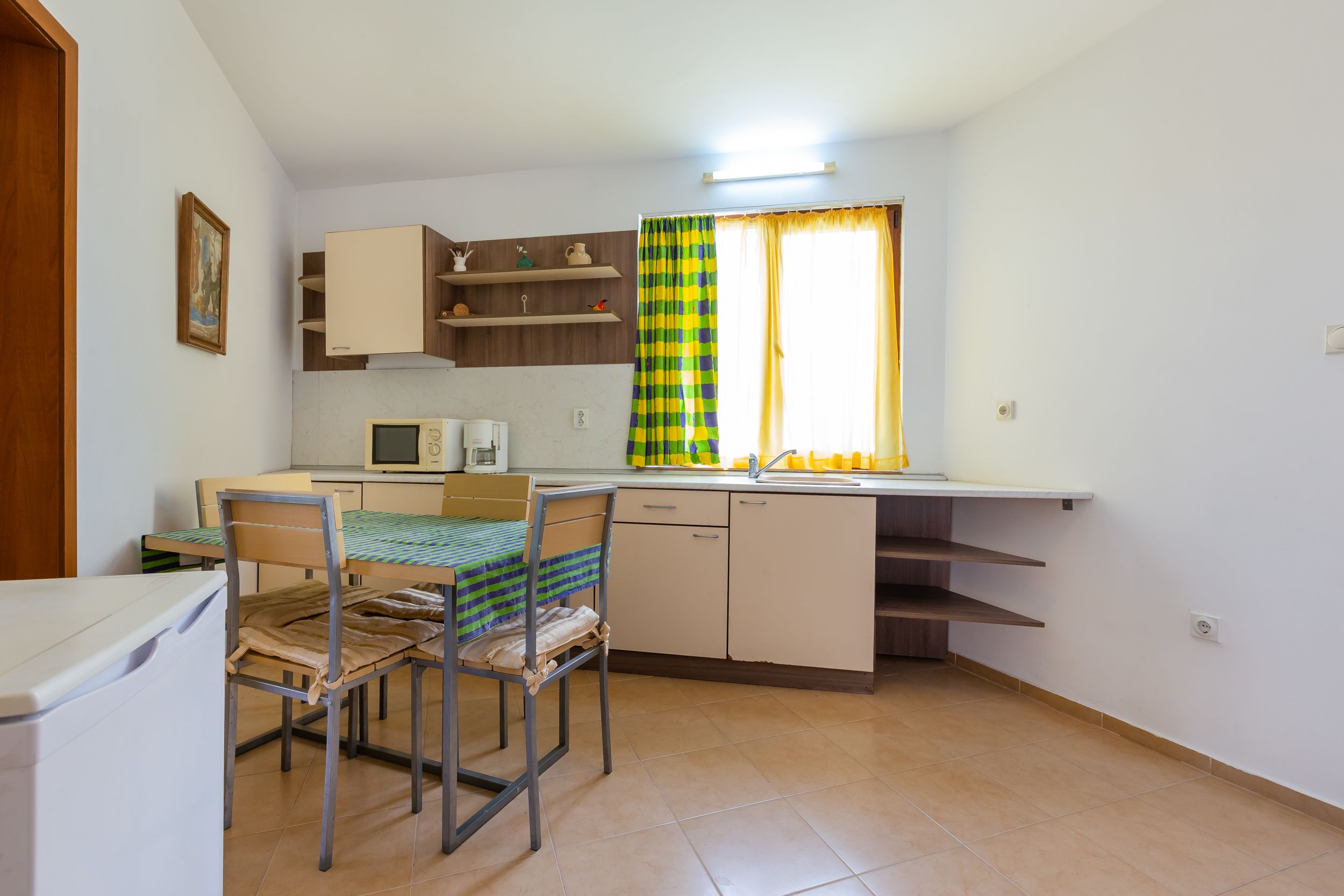 A compact kitchen with a dining area, a microwave, and a window with curtains.