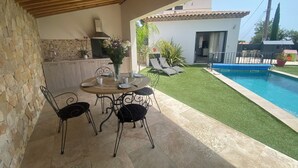 An outdoor patio with a round table and chairs, a stone wall, a kitchen area, and a swimming pool. - Provencal detached villa (La Gaude)