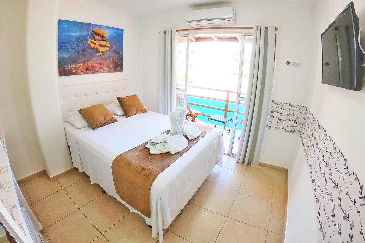 A hotel room with a bed, a painting, a TV, and a balcony with a pool view.