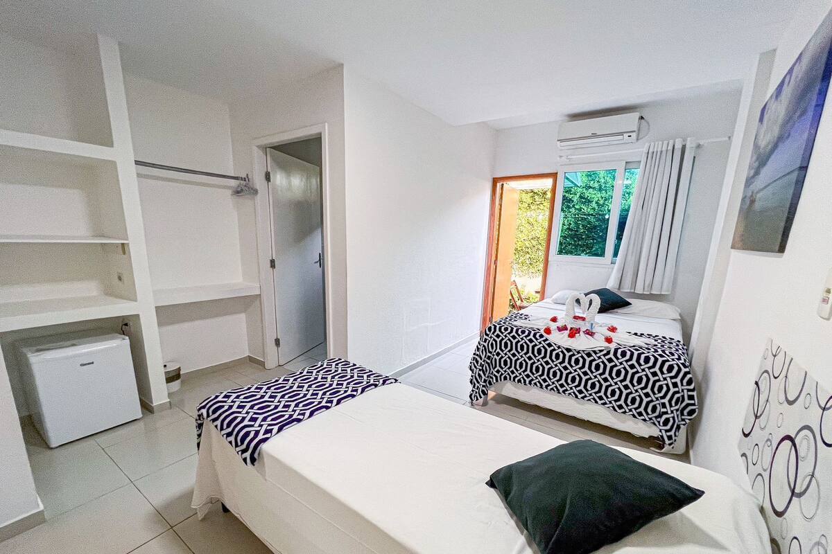 A bedroom with two beds, a wardrobe, a small refrigerator, and a window with curtains.