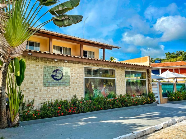 A building with a tiled roof, large windows, and a sign with a logo and website. - Pousada Sereia do Porto (Ipojuca)
