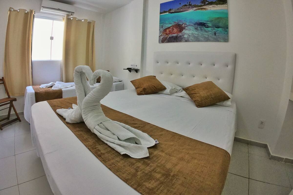 A hotel room with a large bed, a headboard, and a painting of a beach scene on the wall.