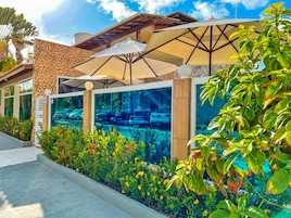 A modern building with large windows, outdoor seating under umbrellas, and a well-maintained garden with colorful flowers.